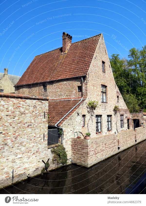 View from the bridge to the beguinage with old stone wall and old brick building with pointed gable in front of blue sky in the sunshine in the old town of Bruges in West Flanders in Belgium
