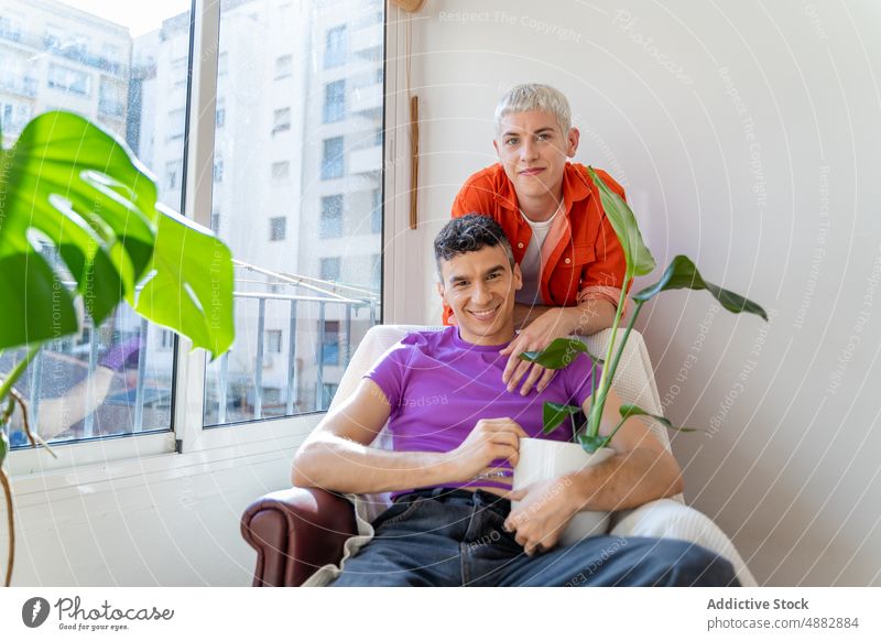 Smiling Gay Couple Sitting On Armchair At Home Love Embrace Arm Around Makeup Fashion Happy Portrait Together Bonding Queer Pride Individuality Lifestyle
