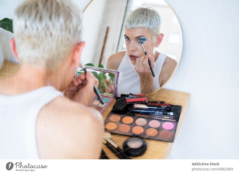 Transgender Man Applying Mascara Eye Shadow Gay Makeup Queer Fashion Individuality LGBTQI Pride mirror Studio Shot Feminine White Background Androgynous Beauty
