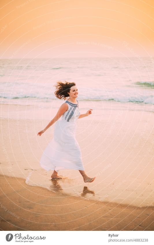 Goa, India. Young Caucasian Woman With Fluttering Hair In Wind In White Dress Walking Along Seashore, Enjoying Life And Smiling In Summer Sunlight Arabian Sea