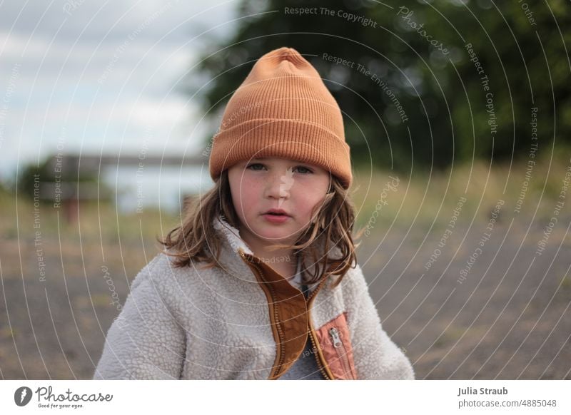 Girl with orange cap Child out Outdoors cuddly jacket outdoor brown hair Freckles Cap stony road Stony Nature Rhön Basalt Wind portrait Exterior shot naturally