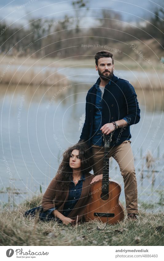 beautiful young hipster couple with guitar by the lake in autumn day man lifestyle outdoors nature landscape sitting family woman view holding love music