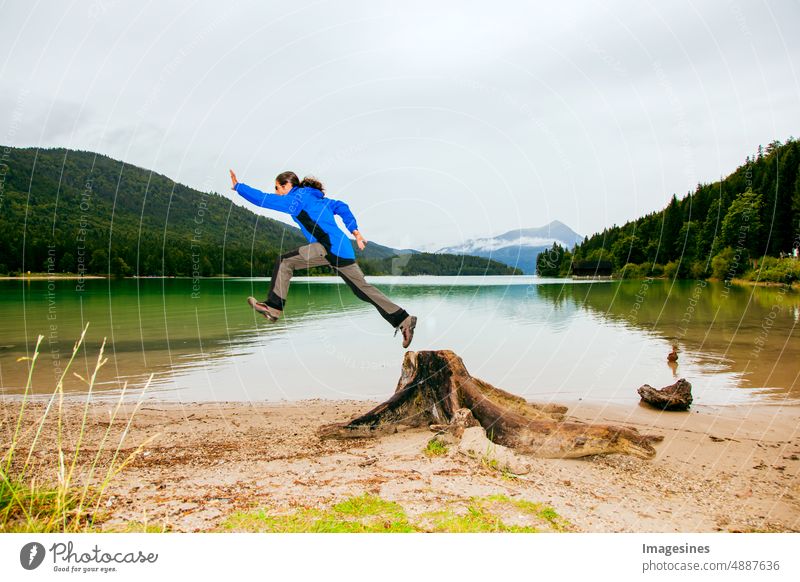 Man jumps from a tree trunk. Bavaria Walchensee on a rainy day. Tree trunk in the foreground. European Alps in Germany, Europe Bavarian Prealps Adventure