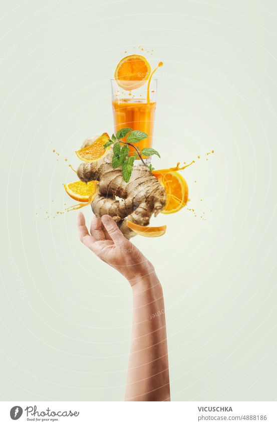 Women hand holding balancing ginger and orange immunity boosting drink with splashing and ingredients at light background. women creative healthy lifestyle