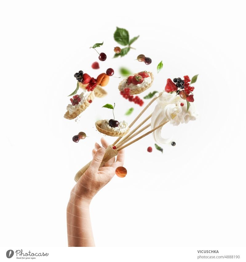 Creative cake baking concept with women hand and flying baked pastry items, fruits, whipped cream and whisk at white background. creative levitation food