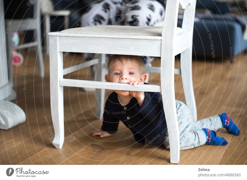 a little baby boy is playing under a white chair in the family living room cute child kid toddler home indoors happy childhood alone lifestyle floor flooring