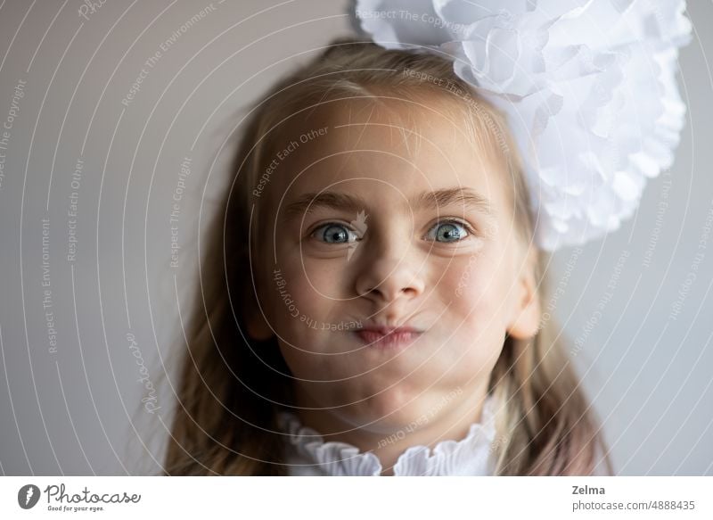 a funny little girl with puffy cheeks and a white bow in her hair face grimace child blue eyes portrait real people caucasian female schoolgirl primary school