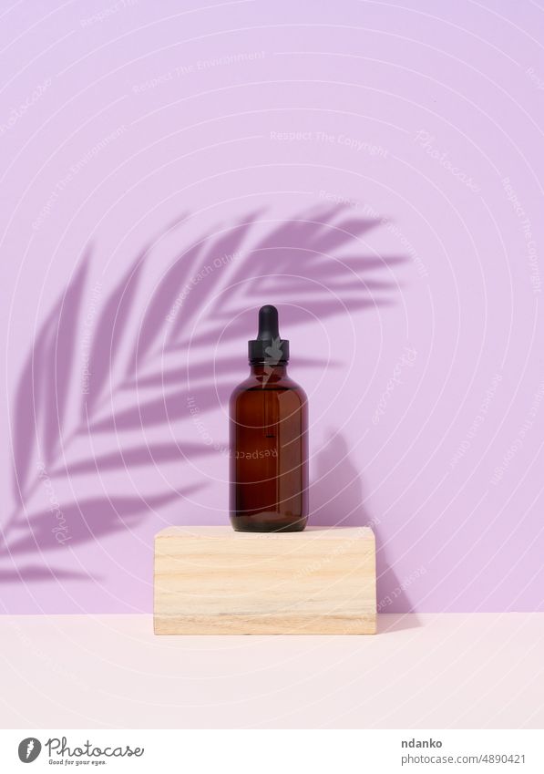 Brown glass bottle with a pipette on purple background. Palm leaf shadow body care podium cosmetic dropper skin care palm product wellness wooden aroma