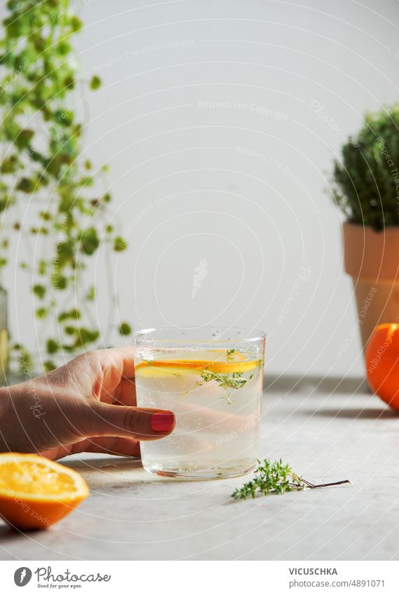 Woman hand holding glass with homemade lemonade with orange and thyme woman kitchen table refreshing summer drink citrus fruit herb front view background cold