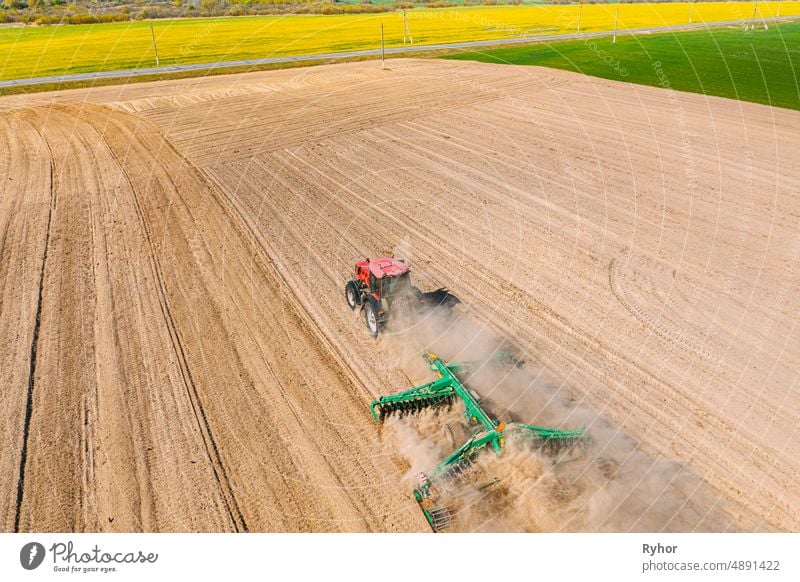 Aerial view. Tractor plowing field. Beginning of spring agricultural season. Cultivator Pulled By A Tractor In Countryside Rural Field Landscape. Dust rises from under plows