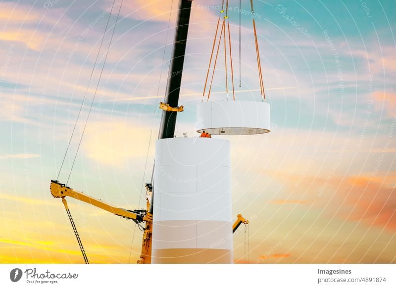 Construction and assembly of a wind turbine by crane on a construction site. Construction work on the wind farm in Germany. Energy saving concept from the construction of wind turbines with evening sky.