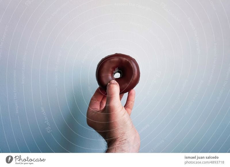 hand holding a chocolate donut, tasty but unhealthy food doughnut pastry breakfast brunch snack sweet food and drink yummy delicious pastries calories bakery