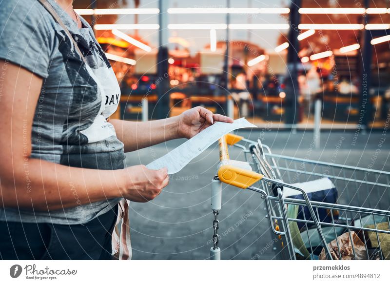 Woman looking at higher prices on receipt after shopping in grocery store. Increasing prices caused by inflation. Higher bills. Economic crisis rise increasing