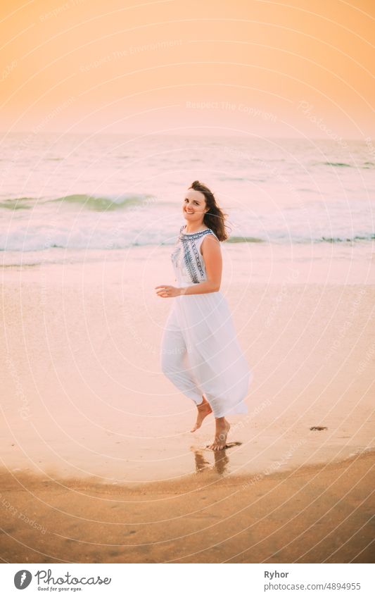 Goa, India. Young Caucasian Woman In White Dress Walking Along Seashore, Looking At Camera And Smiling In Summer Sunlight Arabian Sea Indian Ocean beautiful