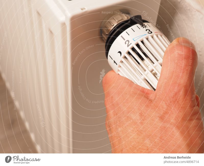 Hand turns the thermostat of a radiator, save energy, reduce energy costs hand comfort energy saving heating costs renewable change climate price rising