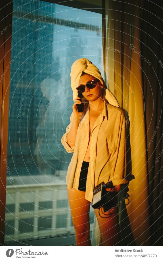 Young lady having phone conversation in hotel room woman talk telephone traveler phone call serious holiday listen relax warm light female young sunglasses