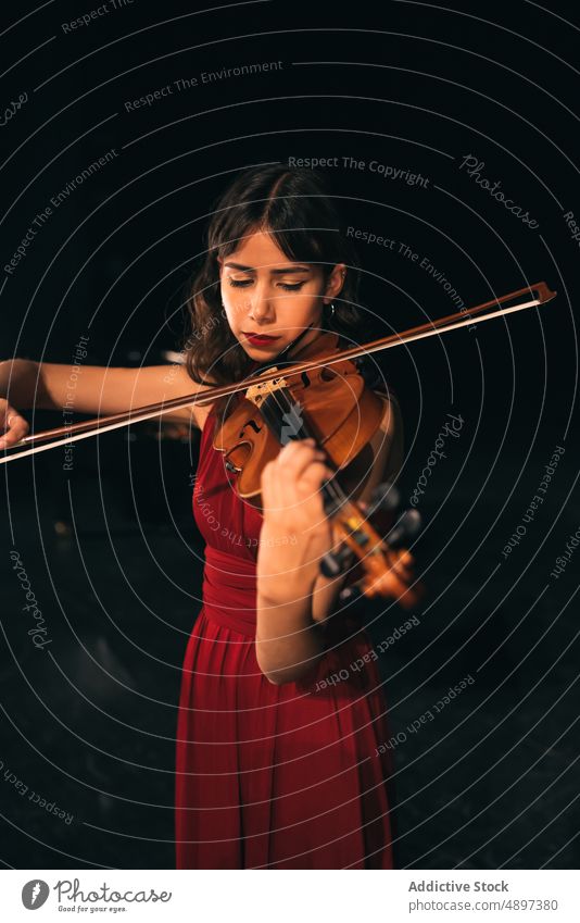 Female musician playing violin on stage woman concert perform theater dark female eyes closed instrument sound melody entertain practice elegant dress tune dim