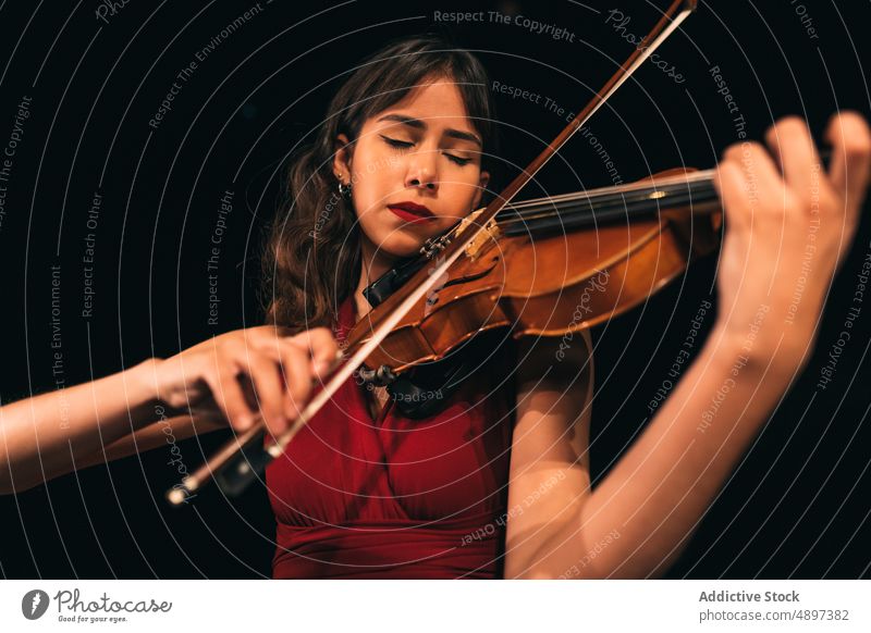 Female musician playing violin on stage woman concert perform theater dark female eyes closed instrument sound melody entertain practice elegant dress tune dim