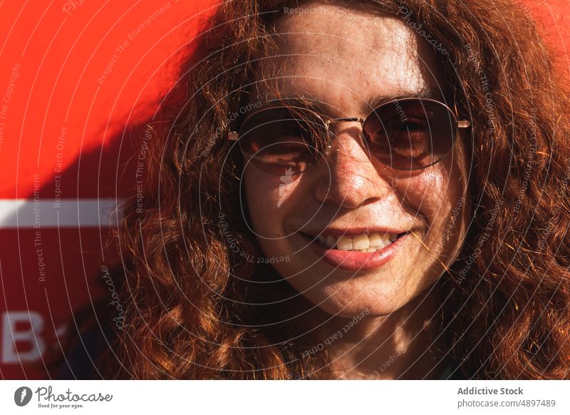 Portrait Of Happy Woman Wearing Sunglasses Smiling Wall Confidence Cool Attitude Sunlight Holding Redhead Curly Hair Beautiful Lifestyle Leisure Happiness