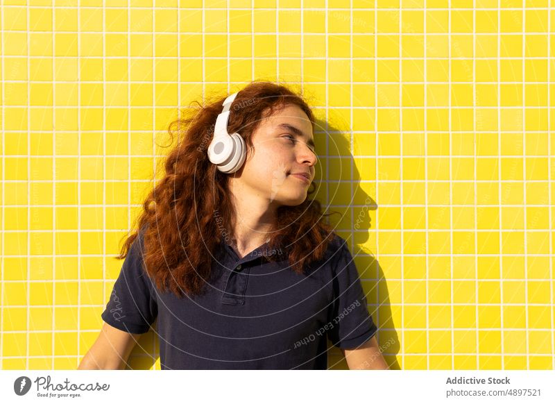 Woman With Headphone Standing Against Wall Headset Looking Away Redhead Yellow Sunlight Tile Tshirt Curly Hair Music Lifestyle Contemplation Beautiful Leisure