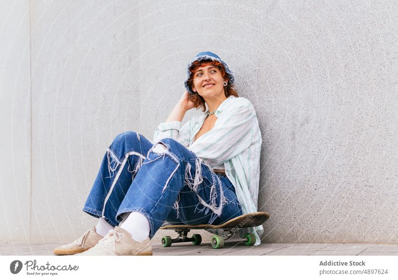 Woman sitting skateboard near wall woman skateboarder hobby sporty content happy pastime smile glad leisure street urban activity enjoy wear casual building