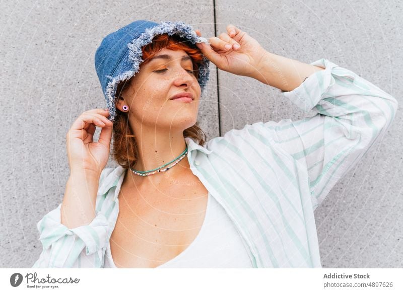 Smiling woman with hat near wall hobby pastime leisure street urban content smile activity enjoy cheerful wear casual building eyes closed attractive summertime