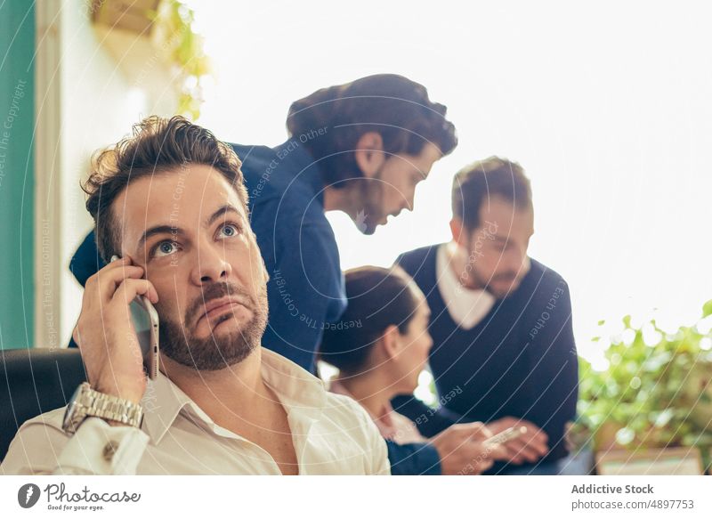 Annoyed man talking on smartphone near coworkers colleague phone call conversation discuss business annoyed unhappy office workspace workplace puzzled confuse