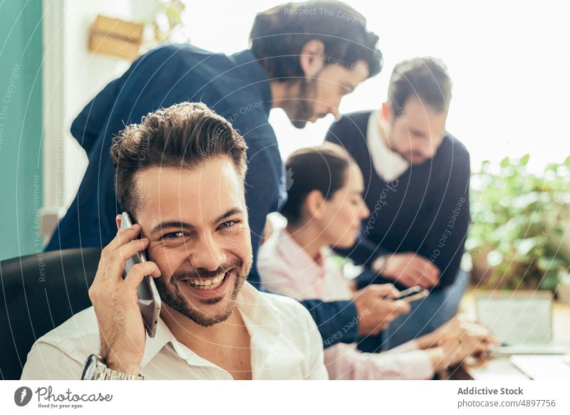 glad man talking on smartphone near coworkers colleague phone call conversation discuss business office workspace workplace puzzled employee communicate