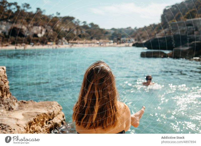 Anonymous lady sunbathing on rocky coast and admiring sea woman relax beach seashore admire holiday enjoy vacation recreation nature female young long hair