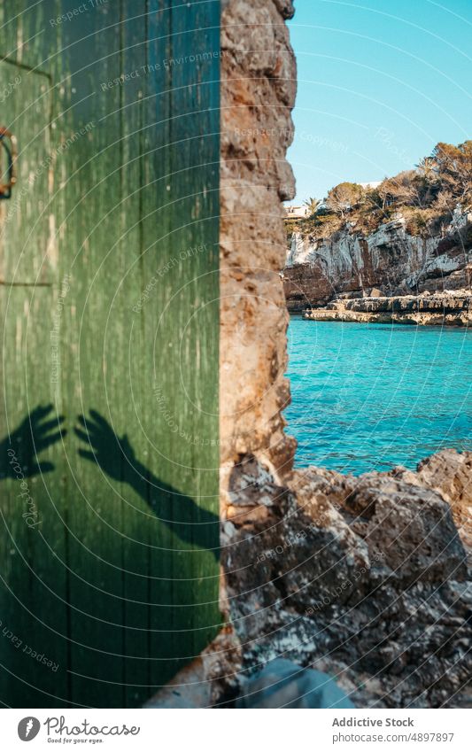 Hands shadows on aged door of stone house on rocky beach in sunlight hand reach out sea holiday couple seashore summer vacation support cliff bay wooden