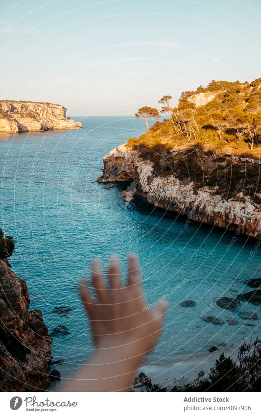 Crop person with outstretched hand on rocky cliff over sea tourist nature seascape landscape scenic reach out traveler island tree viewpoint picturesque seaside