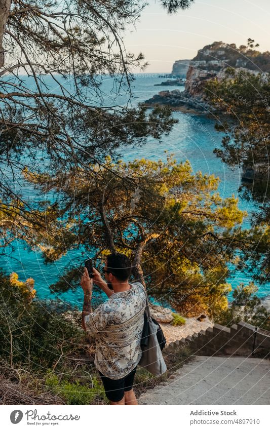 Young male tourist photographing sea on stairs in scenic bay man take photo staircase traveler smartphone vacation beach photography nature seascape holiday