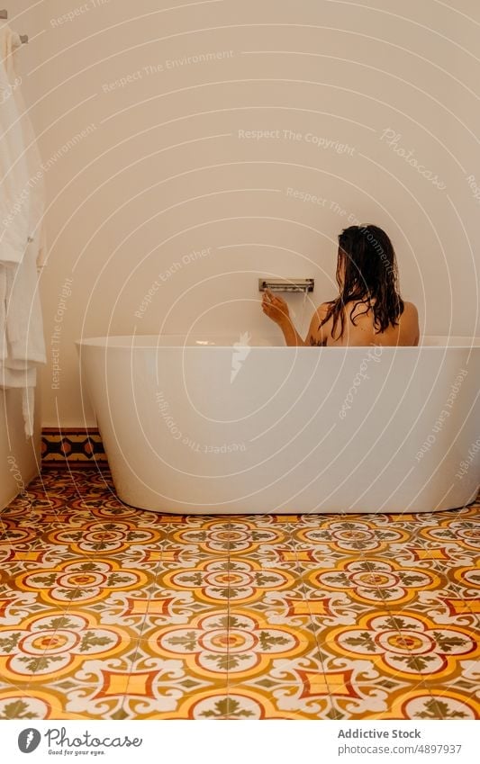 Anonymous woman taking bath in modern bathroom bathtub hygiene azulejo interior washroom wellness body care tile relax female young brunette wet hair