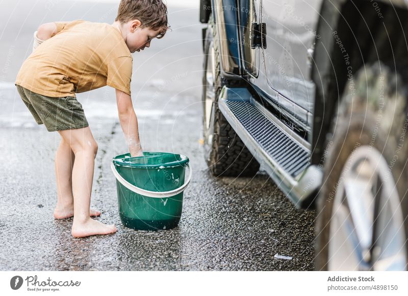 Caucasian Boy Washing Car With Soap Clean Bucket Sponge Sud Foam Lather Lifestyle Standing Outside Self Service Activity Vehicle Transportation Dirty Wet One