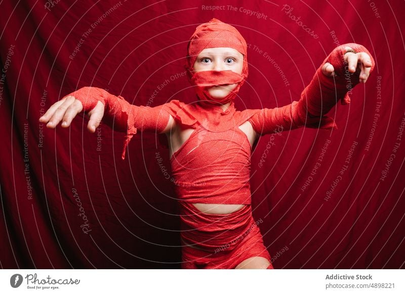 Cute little kid in mummy costume shouting and gesturing in red studio child halloween boy scary portrait spooky reach out make face creepy adorable celebrate
