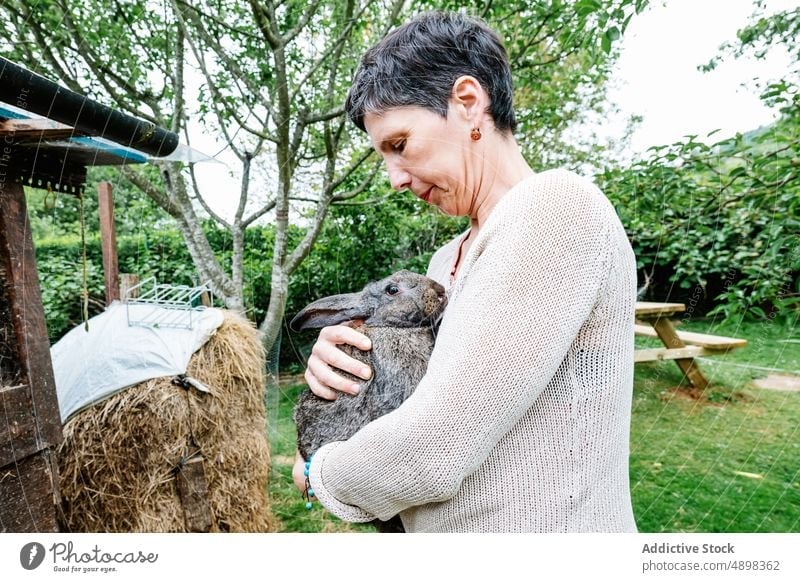 Happy female owner holding cute hare in countryside woman rabbit farmer happy garden embrace backyard animal cheerful middle age short hair dark hair casual