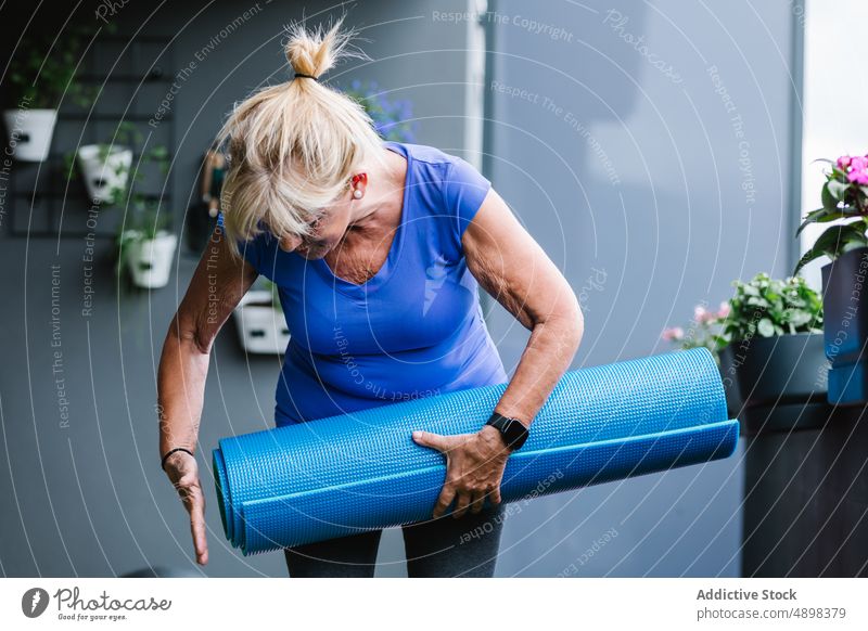 Active Elderly Woman With Rolled Yoga Mat At Gym Senior Fitness Healthy Lifestyle Holding Blue Smartwatch Preparing Workout Sporty Training Body Exercise