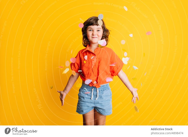 Cheerful girl standing under confetti happy play party smile celebrate fall colorful bright kid casual holiday delight vivid child cheerful birthday event