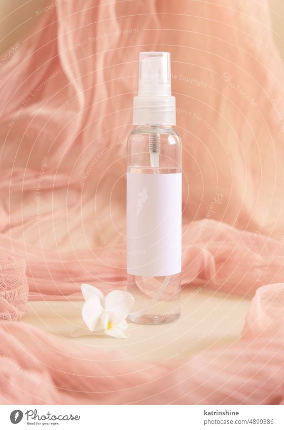 One pump dispenser bottle near white orchid flowers againts light pink tulle. Mockup yellow mockup tropical pastel negative space copy space close up Brand