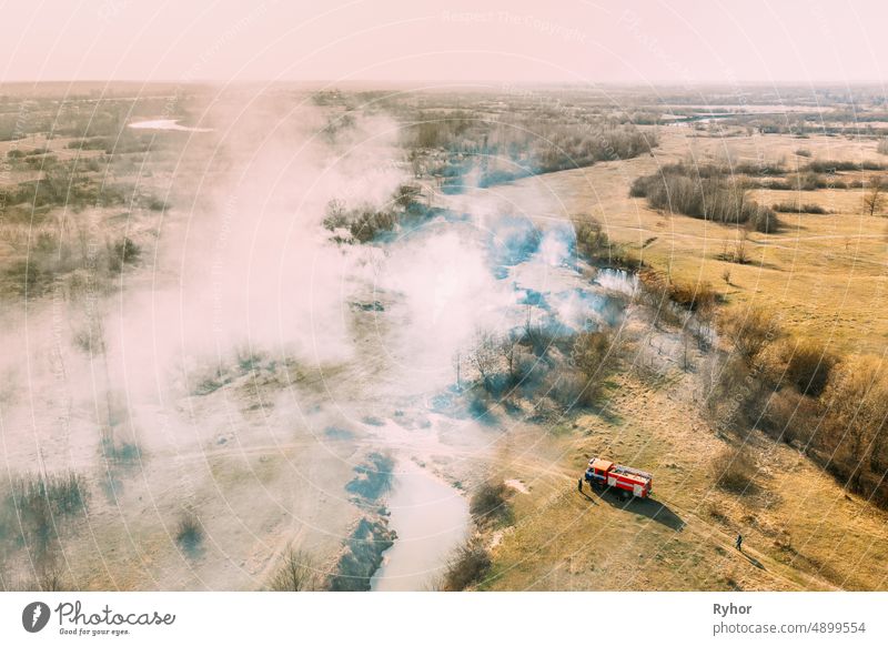 Aerial View. Spring Dry Grass Burns During Drought Hot Weather. Bush Fire And Smoke. Fire Engine, Fire Truck On Firefighting Operation. Wild Open Fire Destroys Grass. Ecological Problem Air Pollution