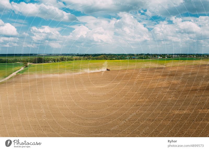 Red Tractor Plowing Field In Spring Season. Beginning Of Agricultural Spring Season. Cultivator Pulled By A Tractor In Countryside Field. Aerial View Rural Field Landscape