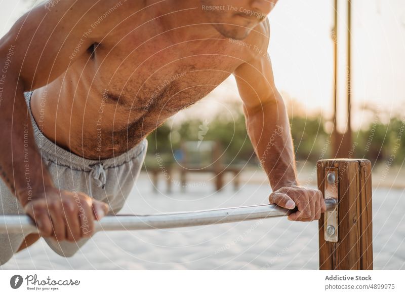 Anonymous sportsman doing bar push ups exercise workout muscle calisthenics determine strong beach hispanic male ethnic latin sand shirtless naked torso athlete