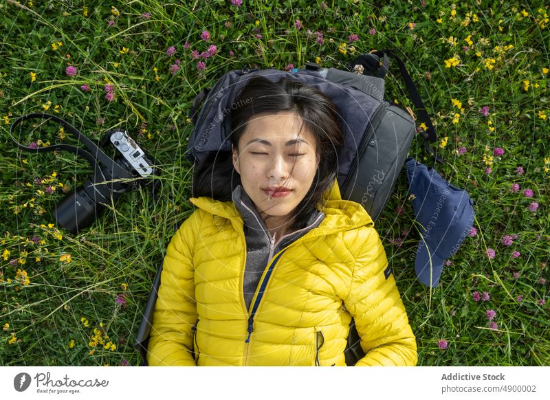 Portrait of beautiful Asian girl lying down on the grass holding Chinese girl Spain active backpack calm camera cap device enjoy europe flowers freedom fun
