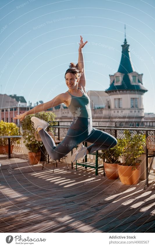 Sportswoman jumping on terrace during training sportswoman exercise happy workout smile healthy lifestyle practice determine move arm raised perform action