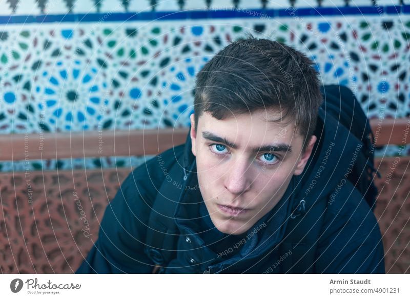 young serious man photographed from above with patterns in the background sitting top shot ornaments wall bench wood portrait teenager looking male beautiful