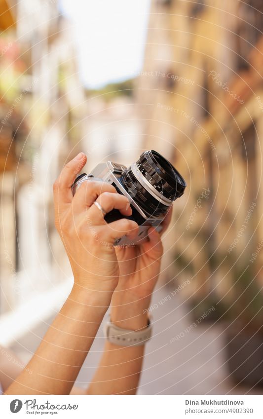 Hands of a person taking photos with a film camera in the streets of old town in Europe. Hands holding photo camera close up, snapping pictures. Digital photo art.  Depth of field. Photographer at work, hobby, traveling and tourism.