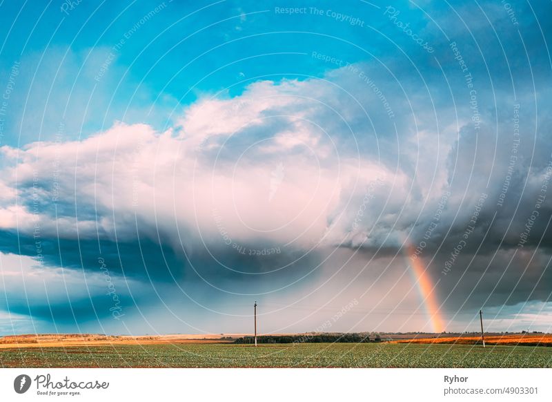 Dramatic Sky During Rain With Rainbow On Horizon Above Rural Landscape Field. Agricultural And Weather Forecast Concept. Countryside Meadow In Autumn Rainy Day