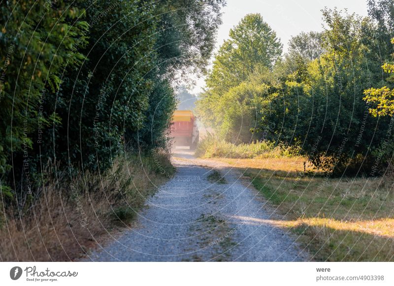 A tractor drives along a dusty dirt road with a hay wagon through bushes to a meadow Road copy space farmer fruit landscape nature organic food plant regional