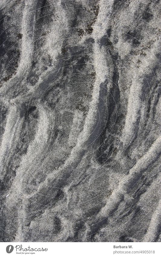 A pattern made by waves on sand at a beach. background closeup outside natural light sandy beach pattern texture of sand grey beige shore shoreline