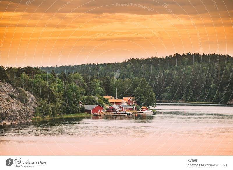 Sweden. Many Beautiful Red Swedish Wooden Log Cabins Houses On Rocky Island Coast In Summer Evening. Lake Or River Landscape apartment archipelago bathhouse